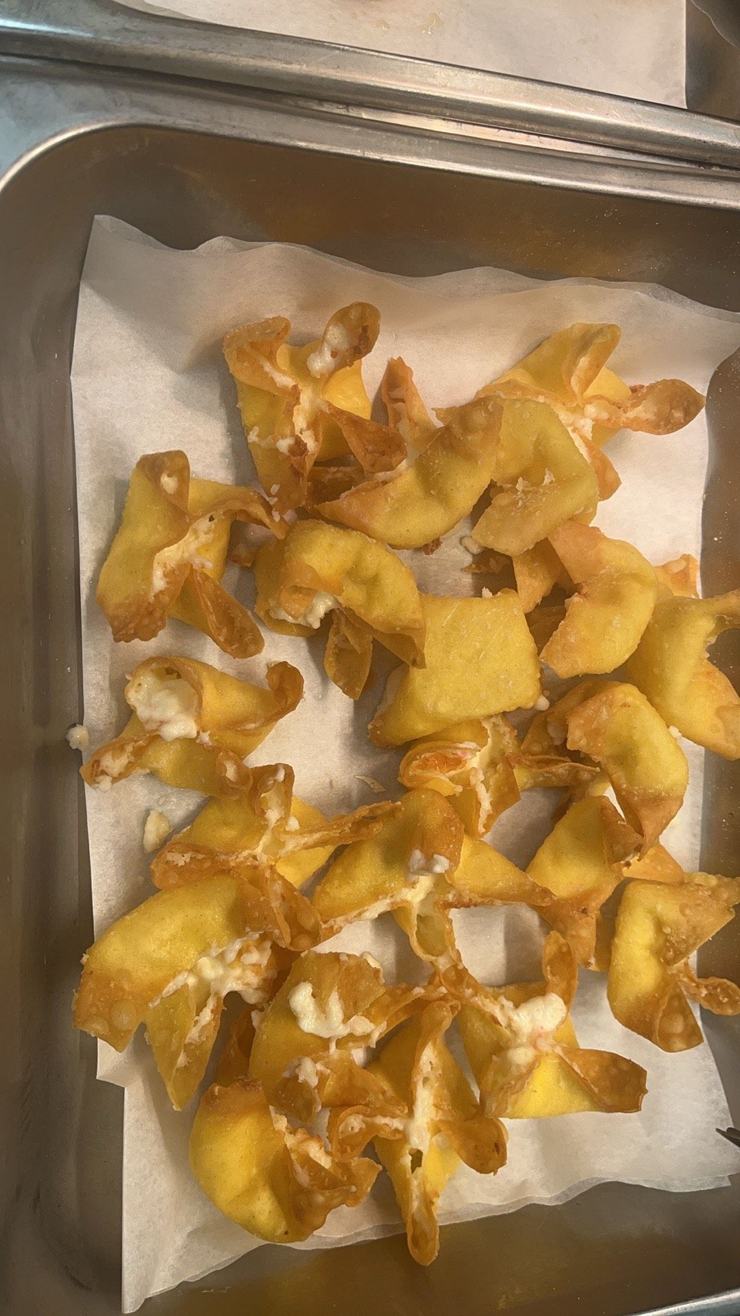 Fried crab rangoons on a white paper towel in a metal tray.
