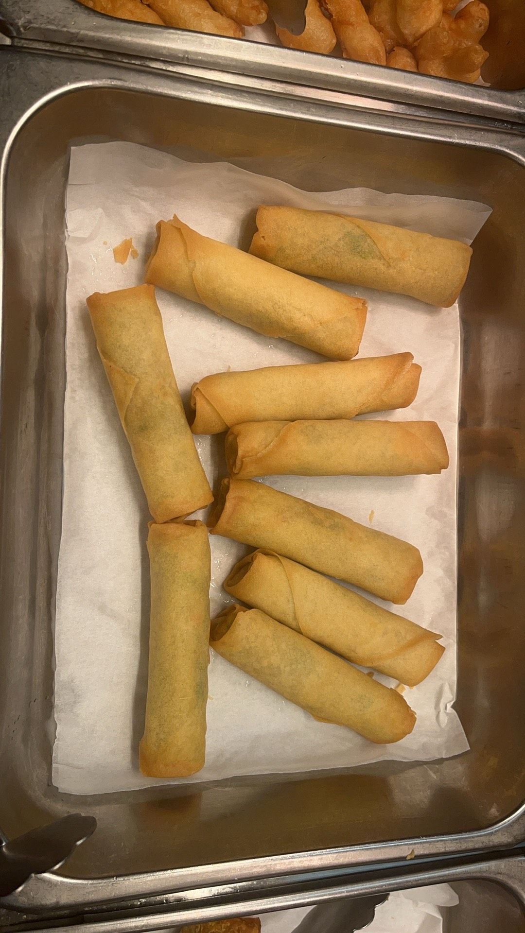 Golden brown spring rolls in a metal food tray, lined with white paper.