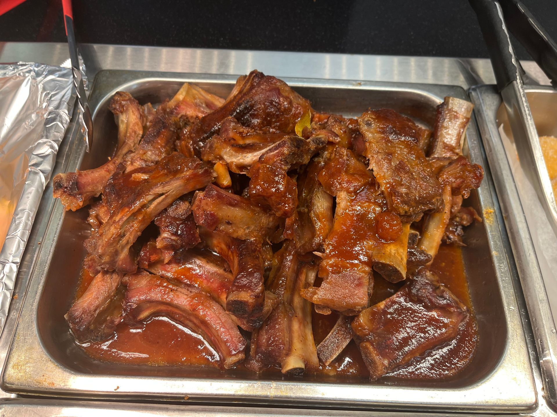 Tray of cooked ribs in a sweet, dark sauce, ready to serve in a buffet.