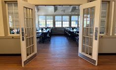 Open double doors reveal a dining room with tables and chairs, hardwood floors, and window views.