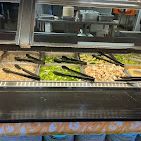 Salad bar with various toppings in stainless steel containers; black tongs.