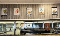 A restaurant's buffet line with framed food art hanging on a wood-paneled wall.