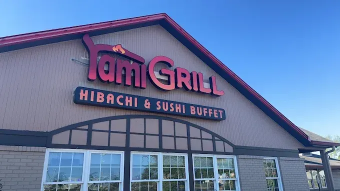 Yami Grill restaurant sign with red and orange lettering against a blue sky. Hibachi and sushi buffet.