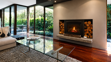 Modern living room with glass walls, a fireplace, stone accent wall, and view of a lush garden