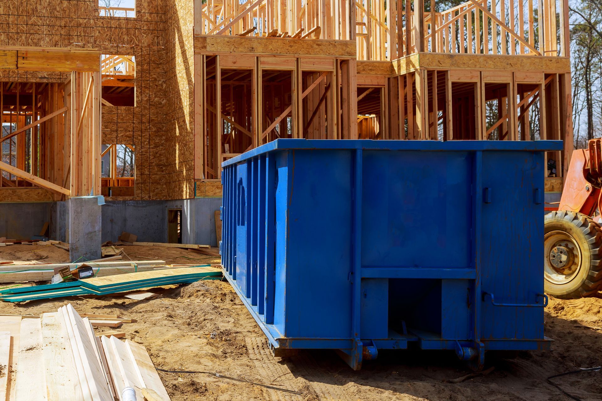 Blue construction dumpster on a building site with wooden framing in the background