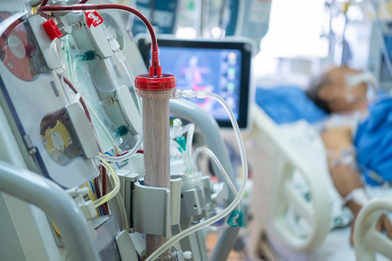 A patient is laying in a hospital bed with a dialysis machine in the foreground.