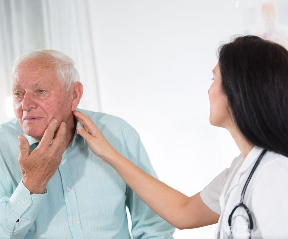 A nurse is examining an older man's throat