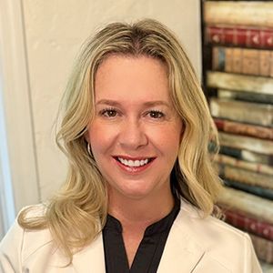 A woman in a white jacket and black shirt is smiling for the camera.