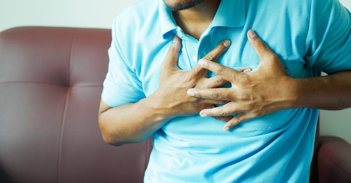 A man is holding his chest in pain while sitting on a couch.