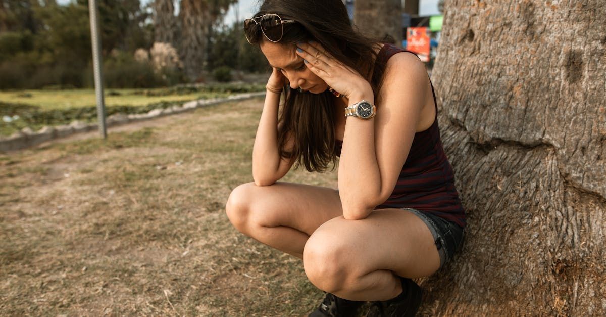 A woman is sitting on the ground leaning against a tree.