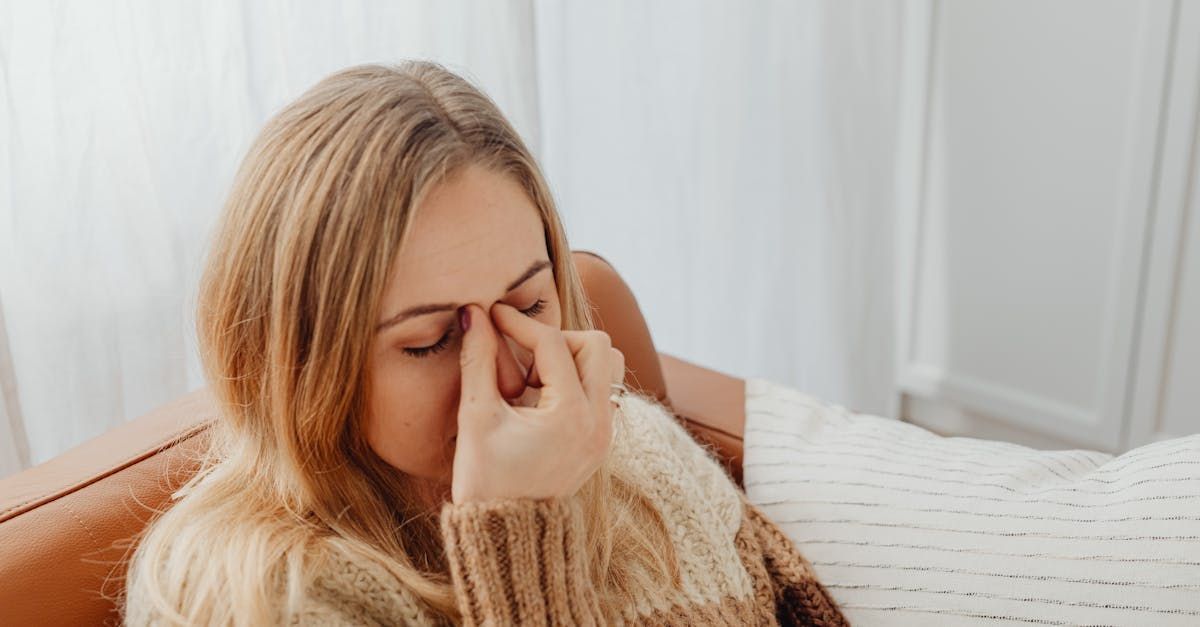 A woman is sitting on a couch with her hand on her nose.