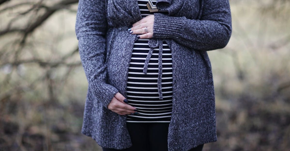 A pregnant woman in a striped shirt is holding her belly.