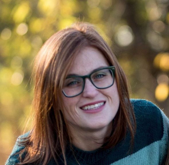 A woman wearing glasses and a striped sweater smiles for the camera