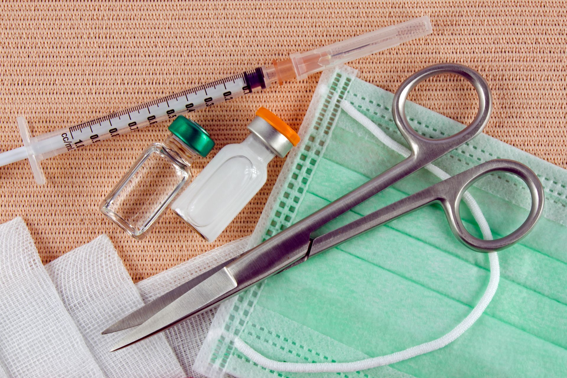 A pair of scissors sitting on top of a mask next to a syringe.