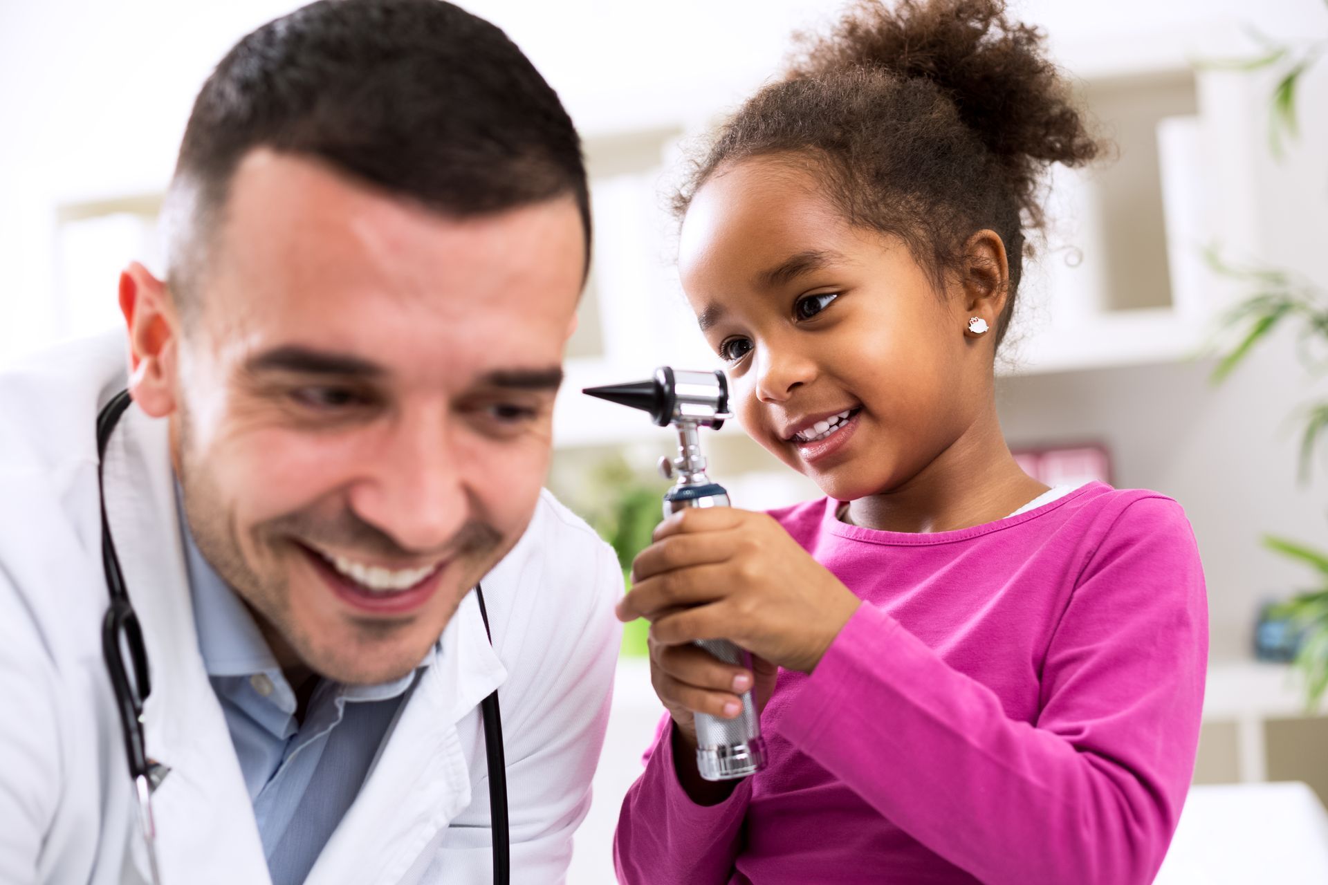 A little girl is looking at her doctor 's ear with an otoscope.
