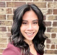 A woman is smiling in front of a brick wall.