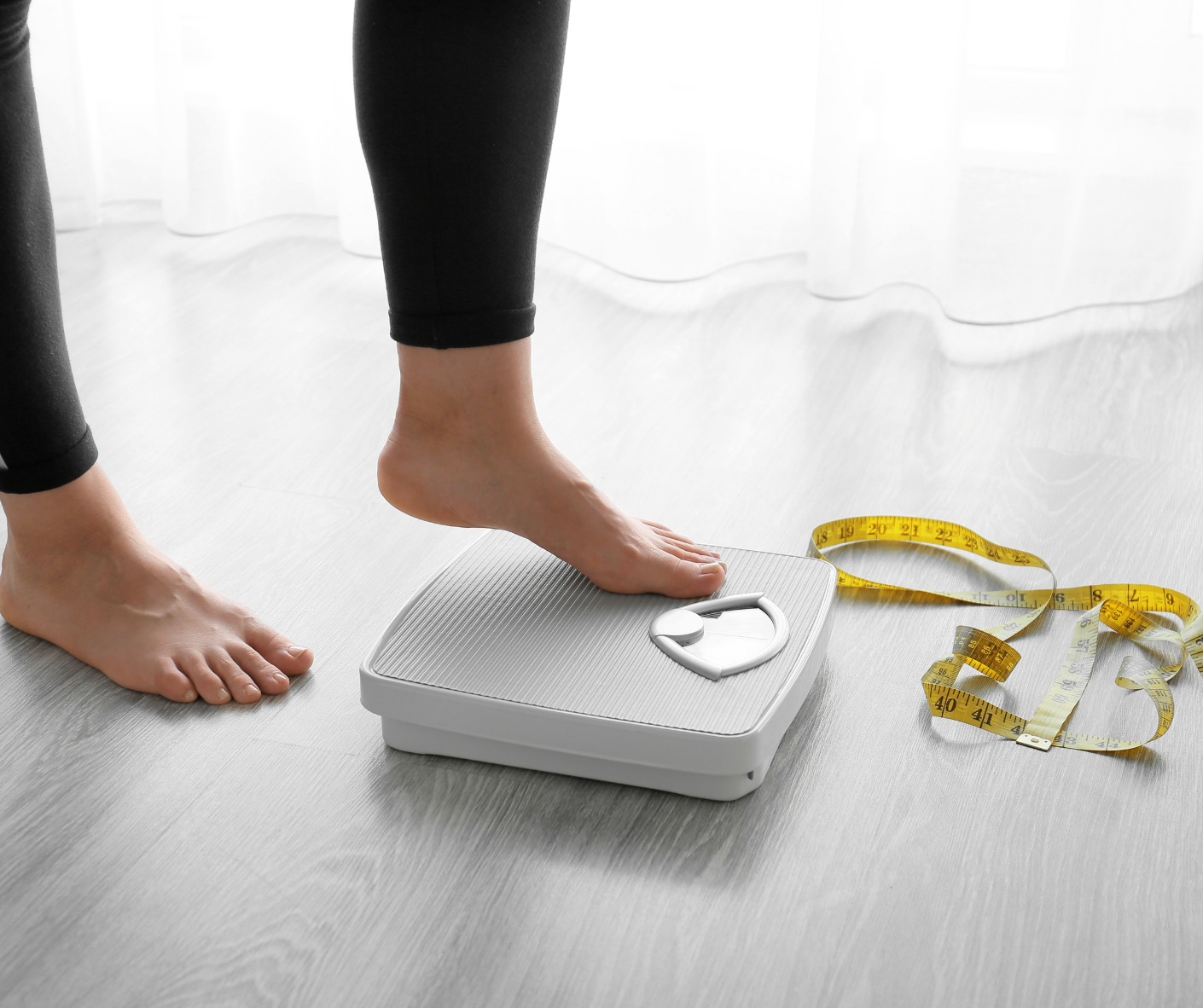 A woman is standing on a scale next to a measuring tape.