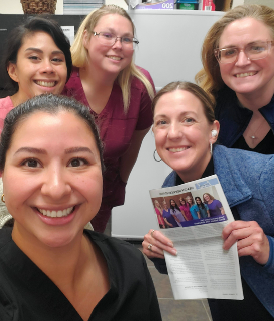 A group of women are posing for a picture and one woman is holding a newspaper