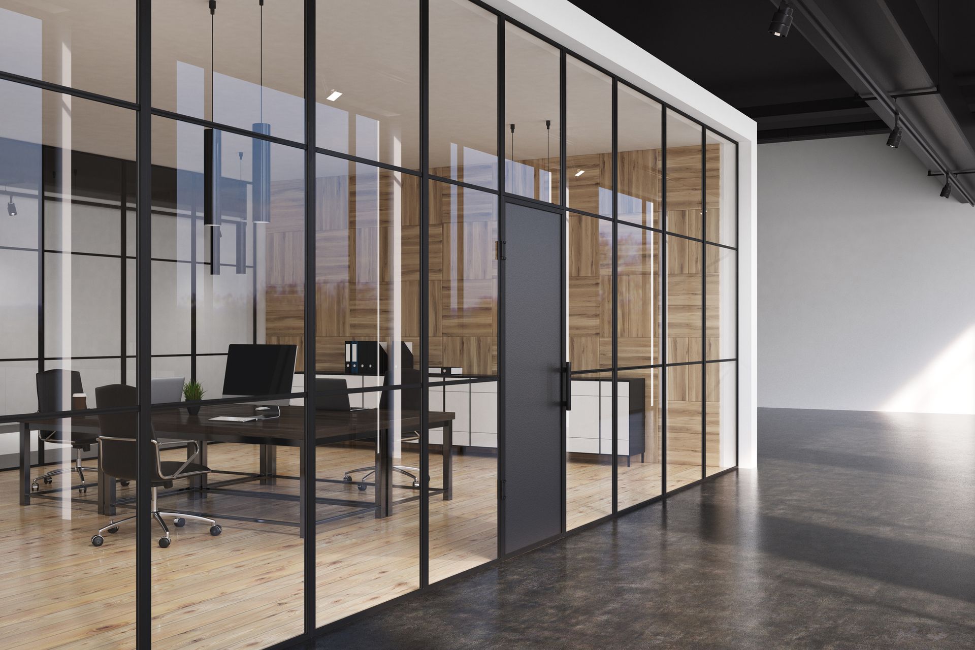 Modern office space with glass-walled meeting room. Black-framed glass panels, dark furniture, and light wooden wall panels. Concrete floor and black ceiling.
