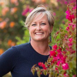 A woman is sitting at a desk with a laptop and a vase of flowers.