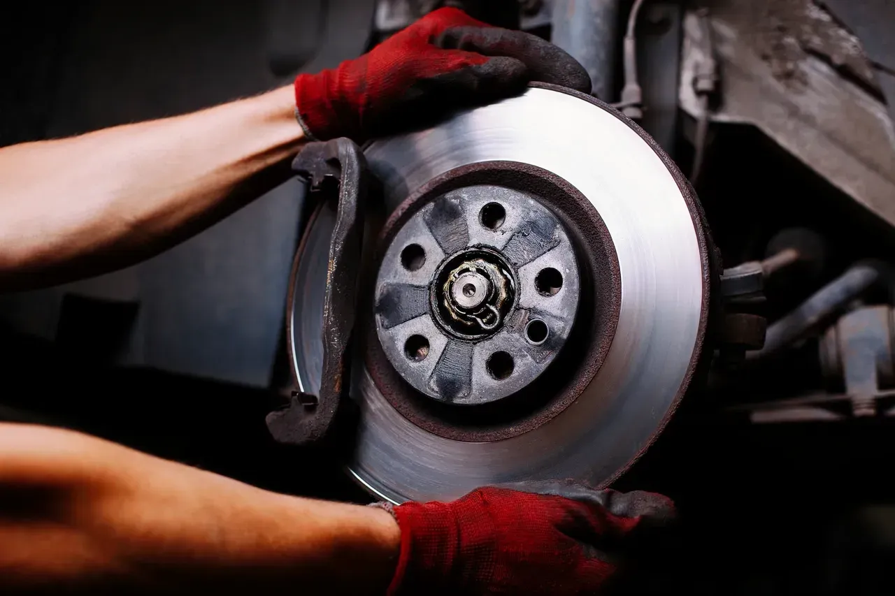 Mechanic wearing red gloves removing a car brake rotor in a workshop