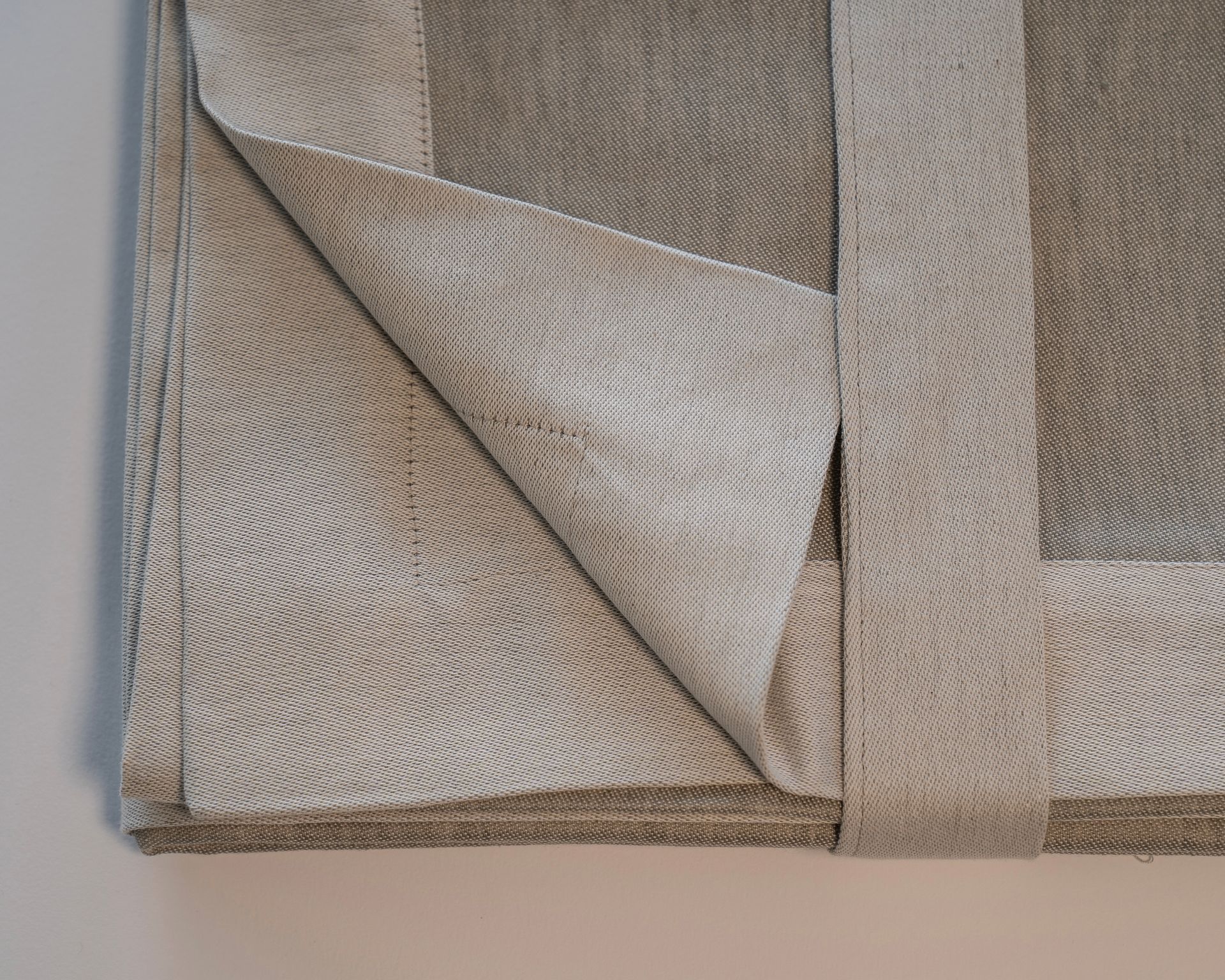 Tessuto beige con bordo a contrasto e angolo ripiegato, che rivela l'interno in tessuto leggero.