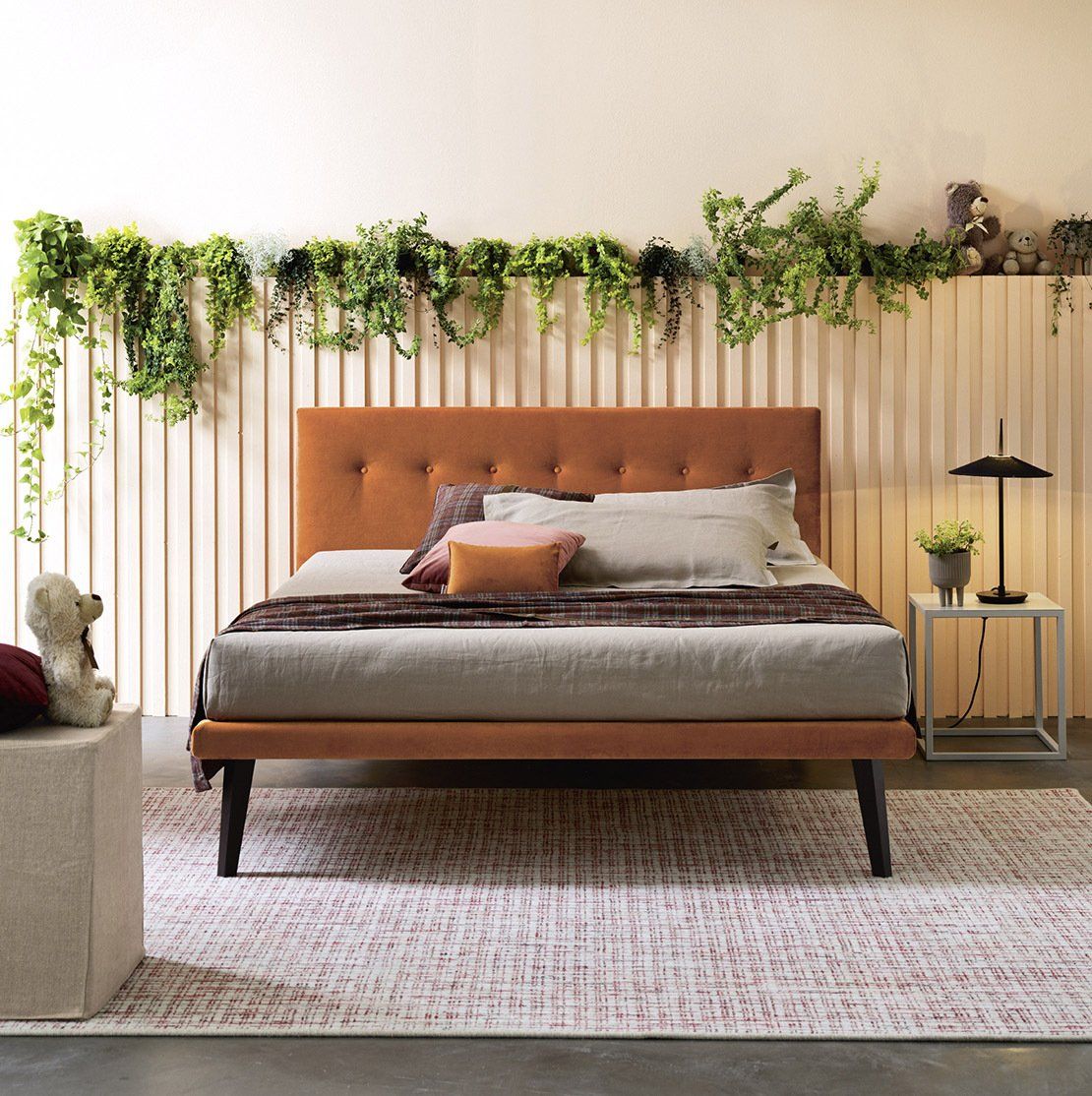 Camera da letto con letto imbottito, piante appese alla parete, un piccolo tavolino e un tappeto a fantasia.