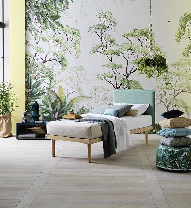 Camera da letto con letto in legno chiaro, carta da parati botanica e pavimento di colore chiaro.