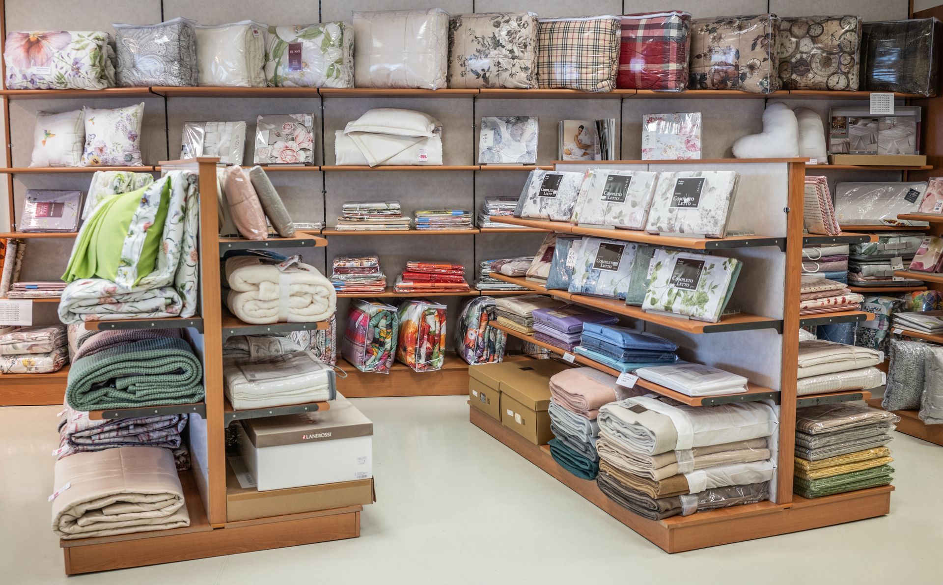L'interno di un negozio di biancheria da letto espone la biancheria ordinatamente impilata e confezionata su scaffali di legno.
