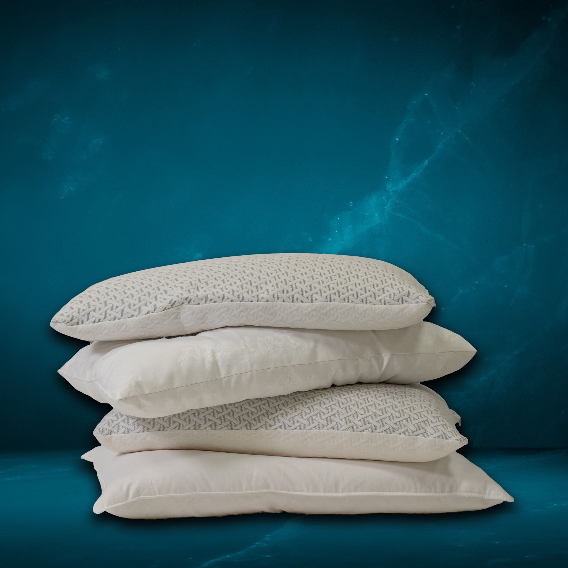 Quattro cuscini bianchi impilati uno sopra l'altro su uno sfondo blu. Due cuscini hanno la parte superiore decorata.