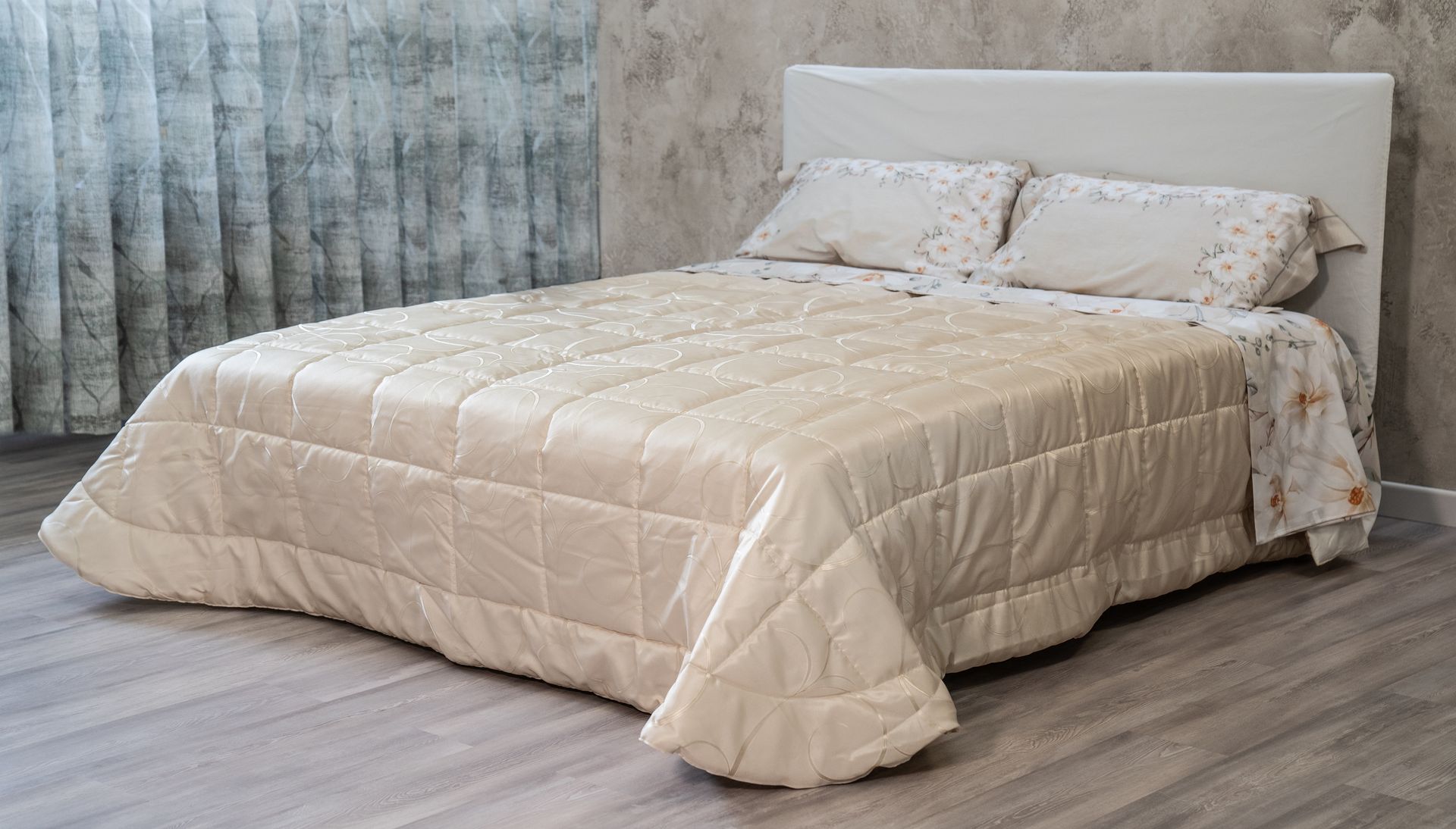 Letto con piumone e cuscini trapuntati color crema, contro una parete e una tenda dai colori neutri.