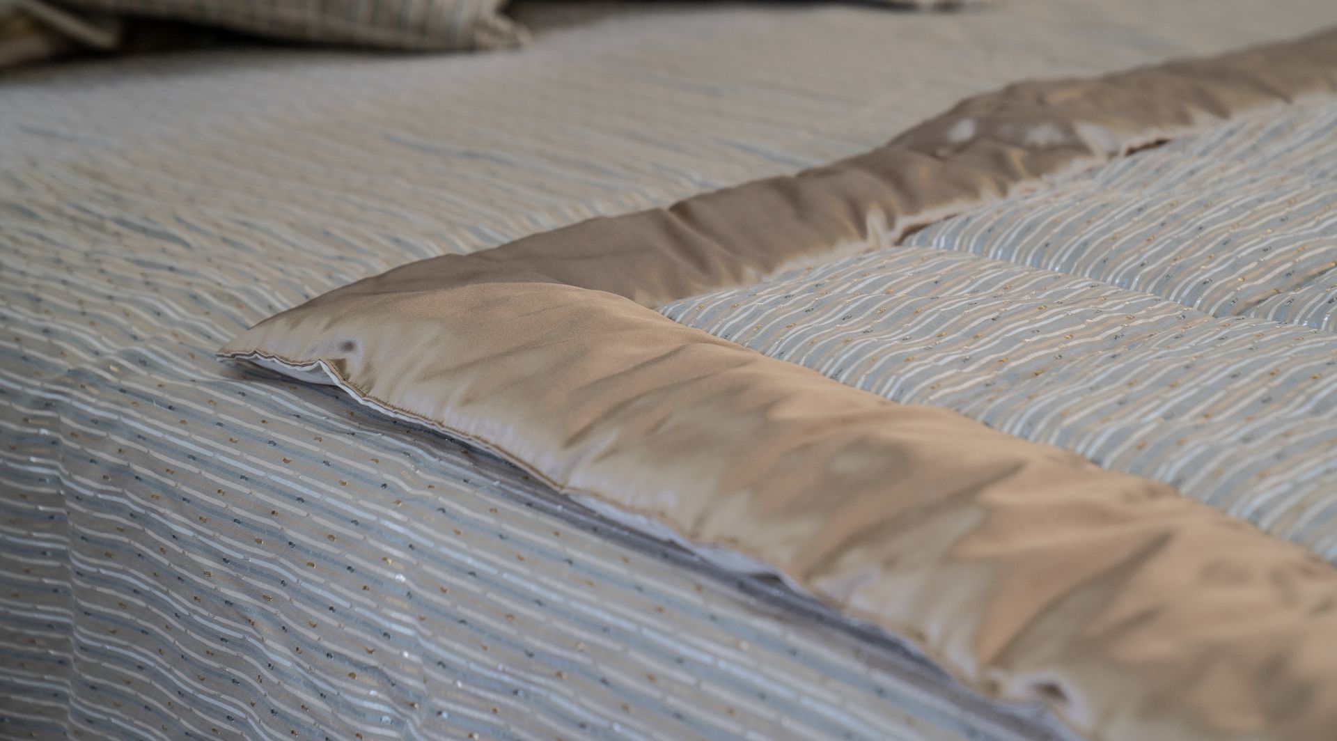 Primo piano di un letto con un piumone a righe bianche e azzurre e un bordo trapuntato beige.