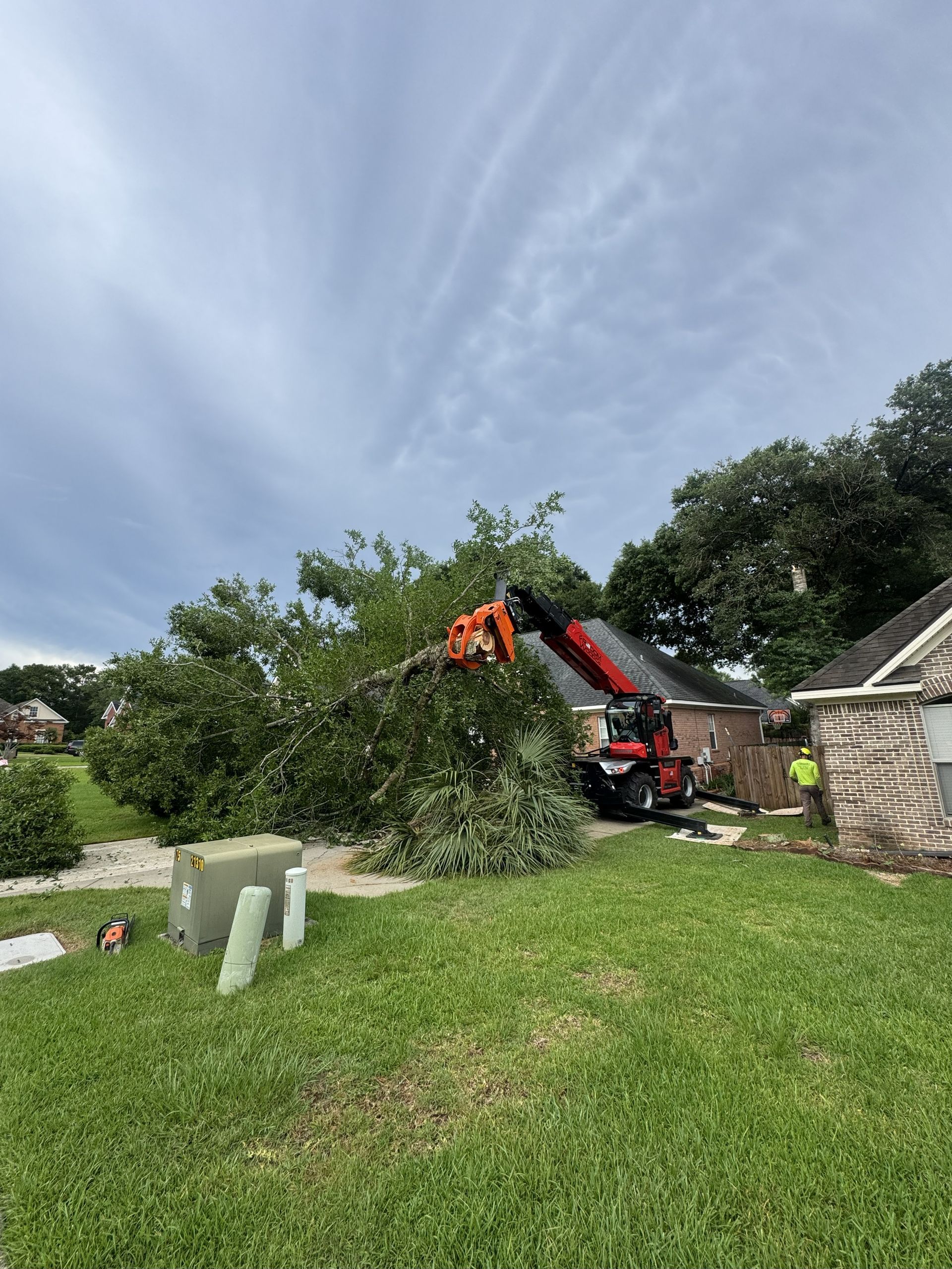 A tree is being removed from a house by a crane on a cloudy day.