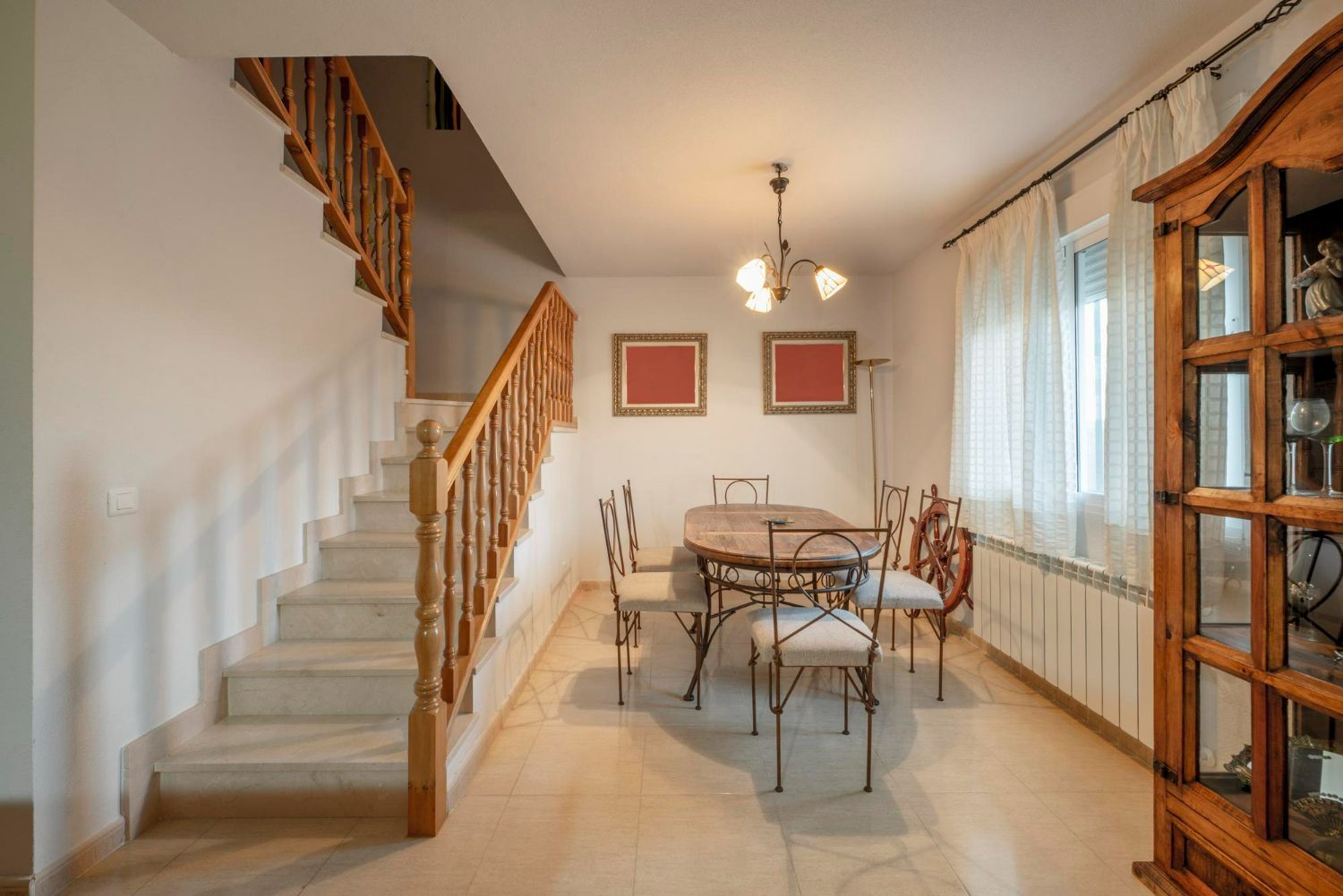 Dining room with a staircase.  Oval table, ornate chairs, chandelier, and a wood cabinet.
