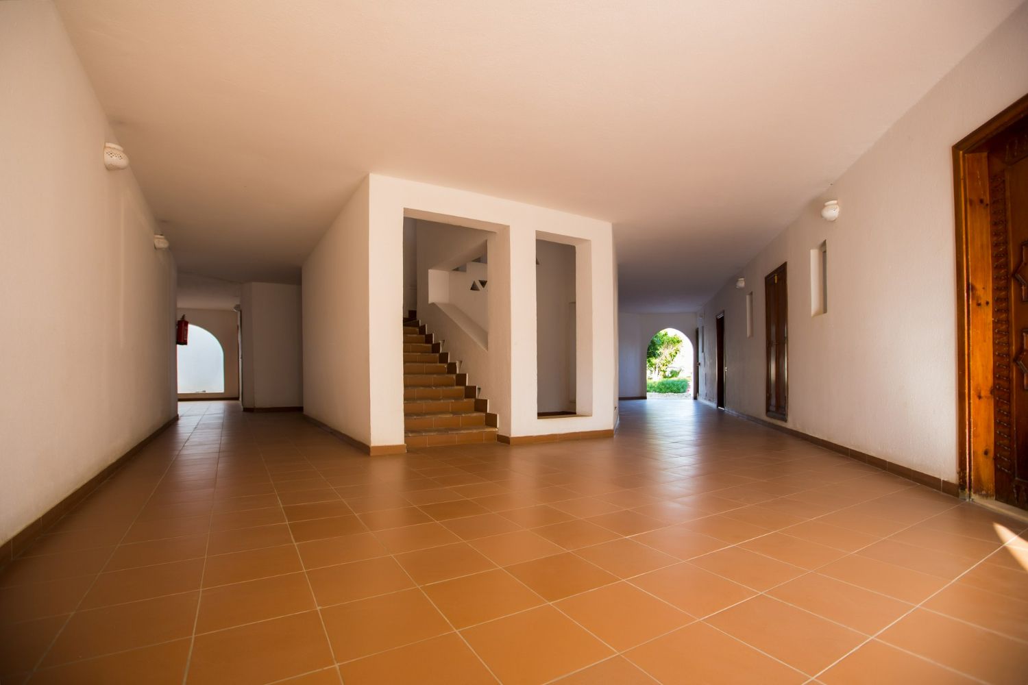 Empty interior hallway with tile floor, stairs, and doorways.