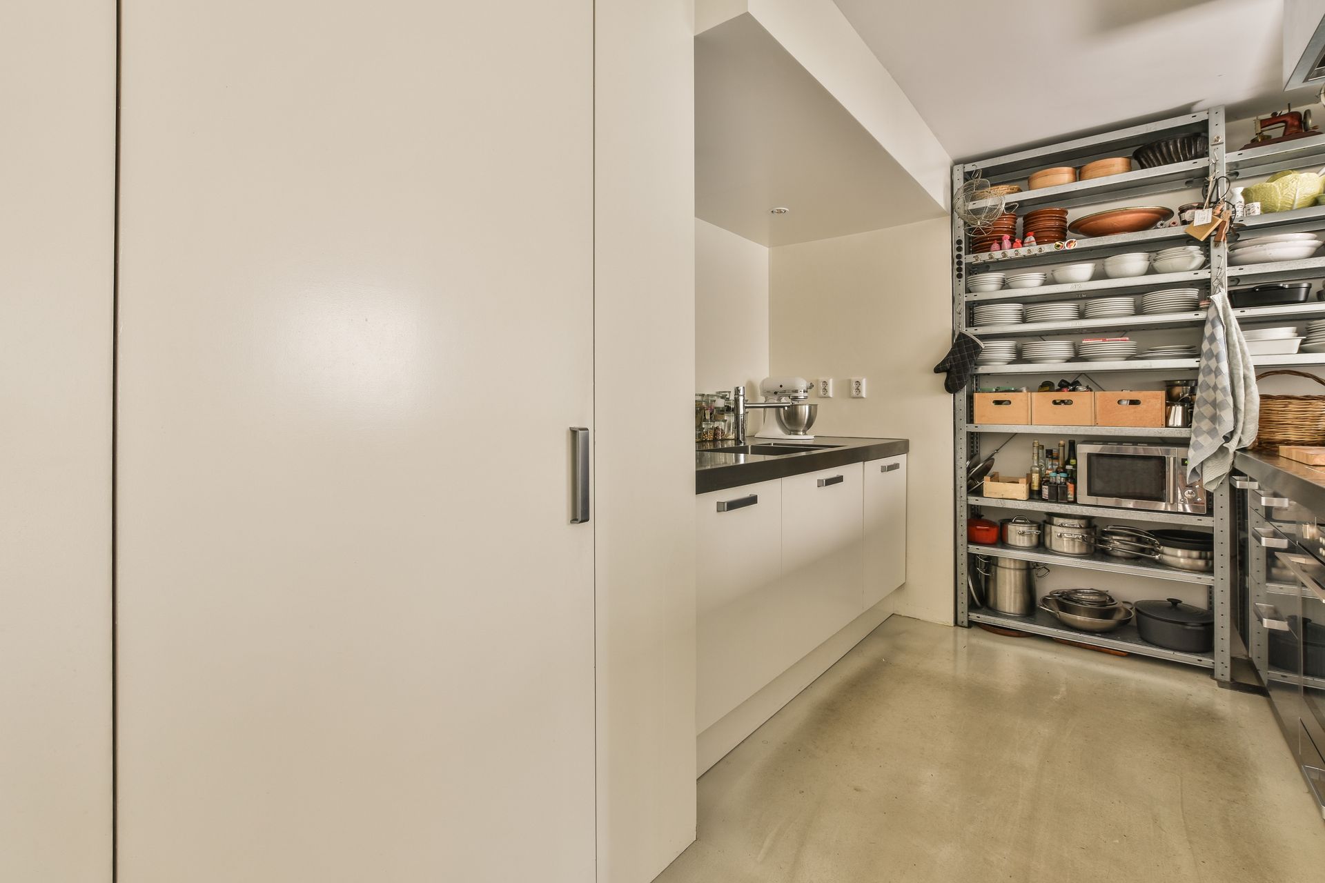 A kitchen with white cabinets and shelves filled with pots and pans