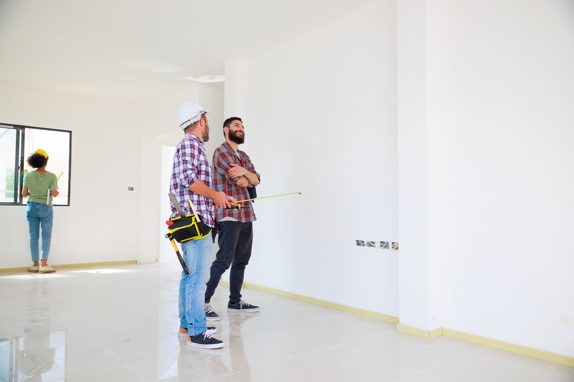 Two men are standing in an empty room looking at a wall.