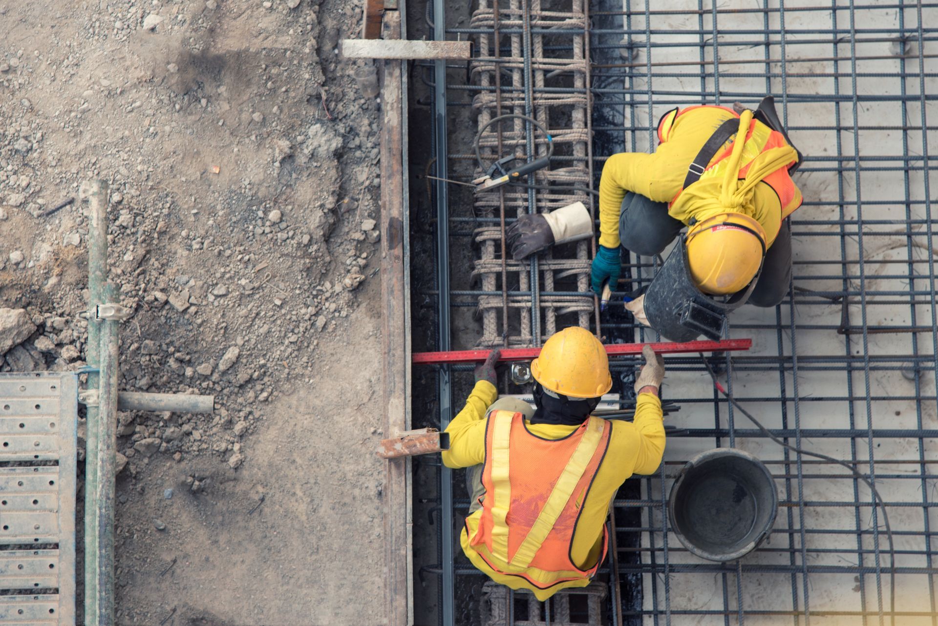 Des ouvriers du bâtiment, vêtus de gilets jaunes et de casques de chantier, travaillent sur une structure en armature.