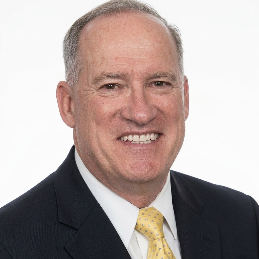 Portrait of a smiling man in a dark suit and yellow tie against a white background