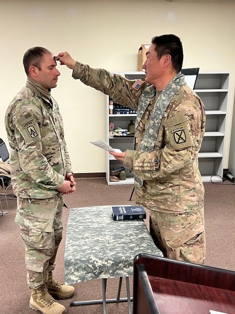 Two soldiers in uniform in an office, one measuring the other's height with a hand up to his forehead.