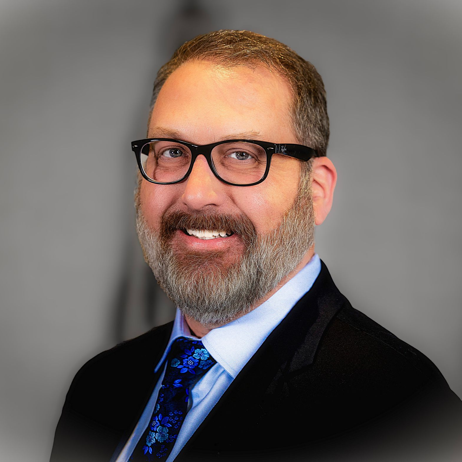 Smiling man in glasses and suit against a gray studio background