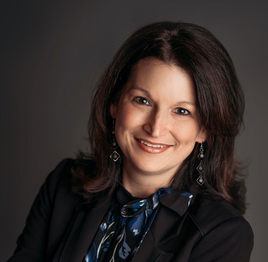 Smiling woman in a black blazer with a blue scarf against a dark studio background