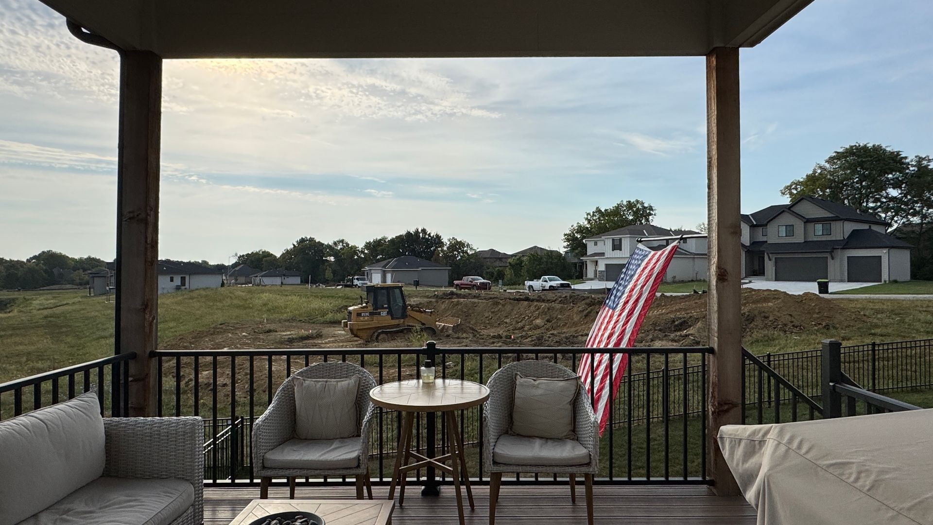 Porch with seating overlooking construction site, American flag, cloudy sky.