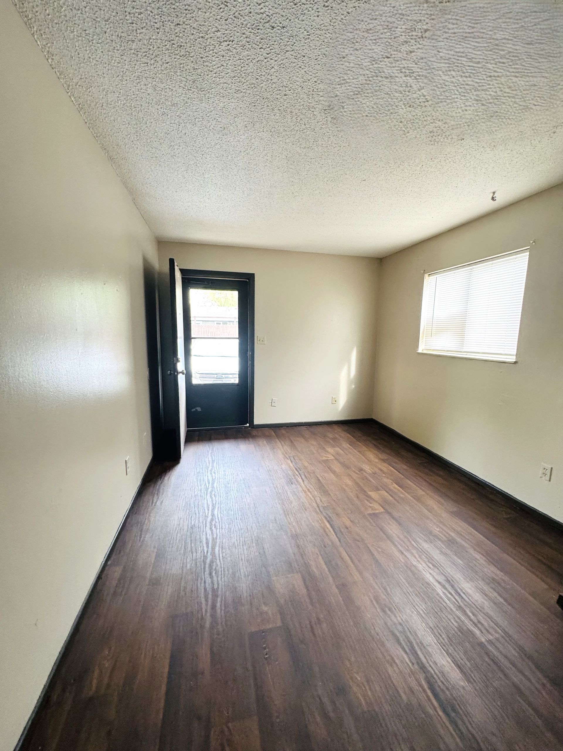 Empty room with dark wood floor, tan walls, and a door and window.