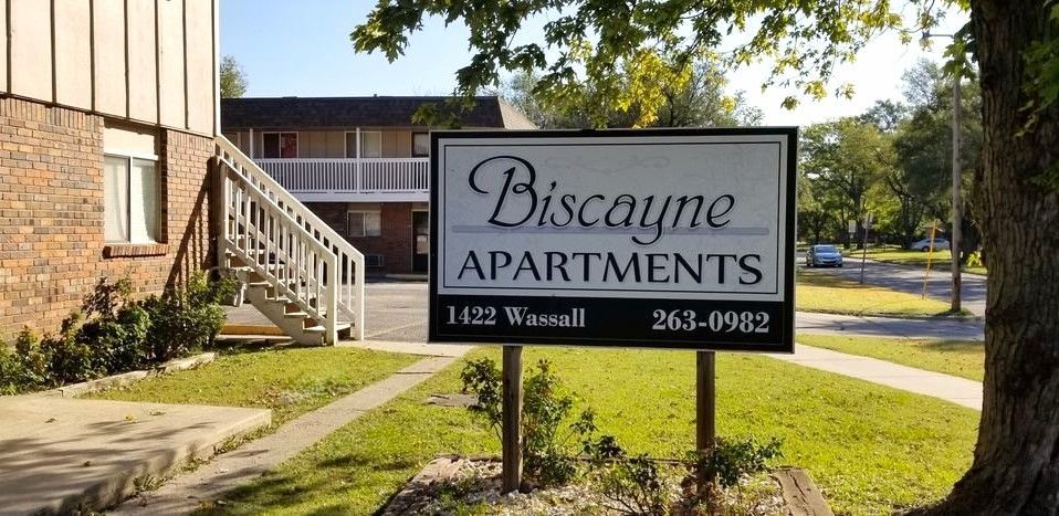 Biscayne Apartments sign with address and phone number, in front of a building with stairs.