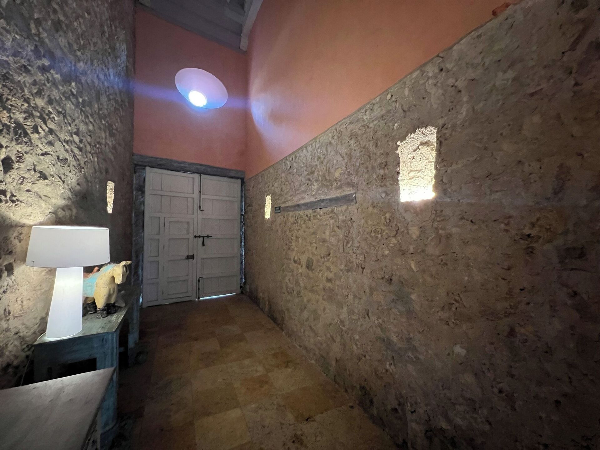 Un largo pasillo con una puerta y una lámpara sobre una mesa.