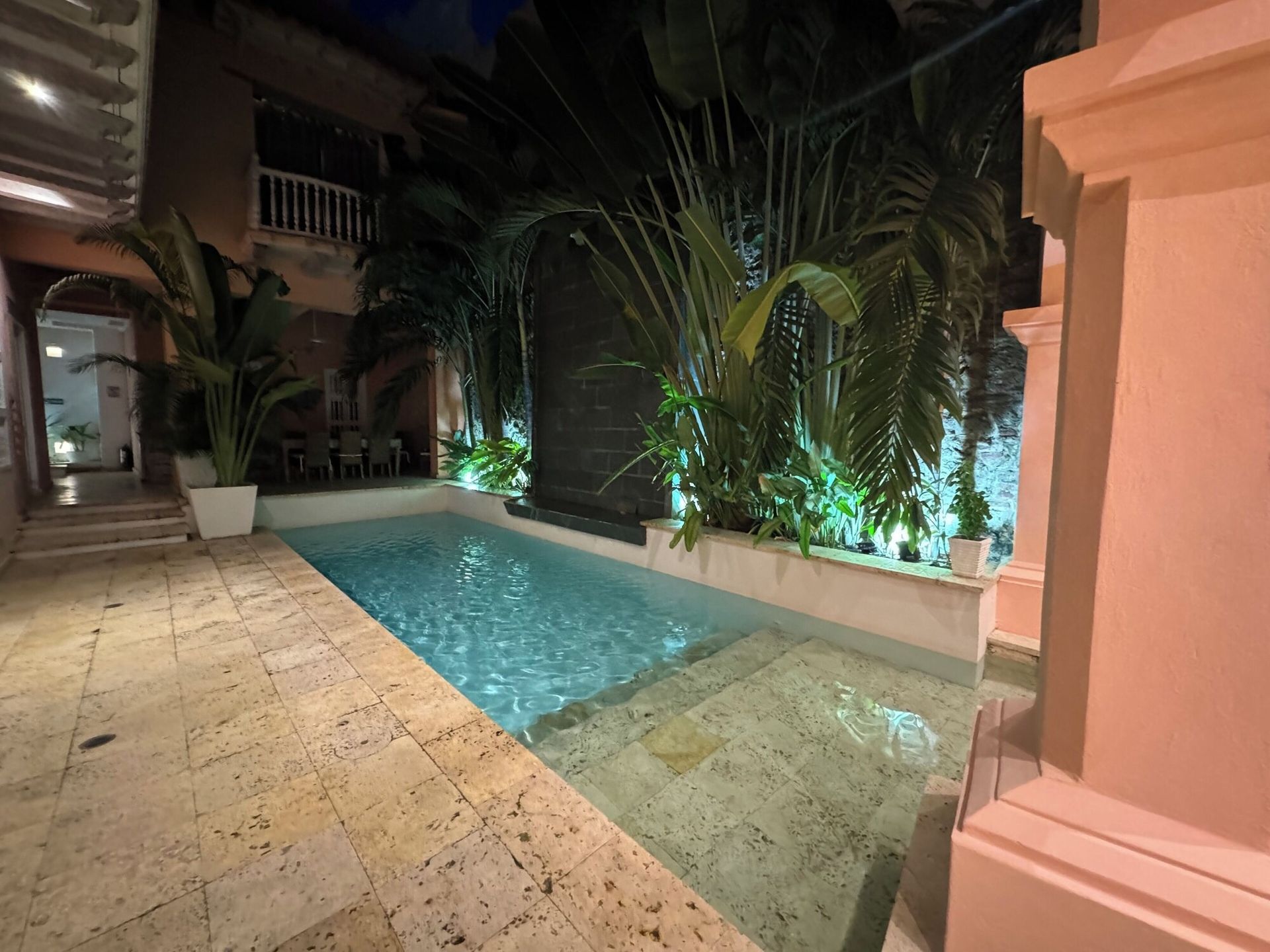 Una gran piscina está rodeada de palmeras y un edificio rosa.