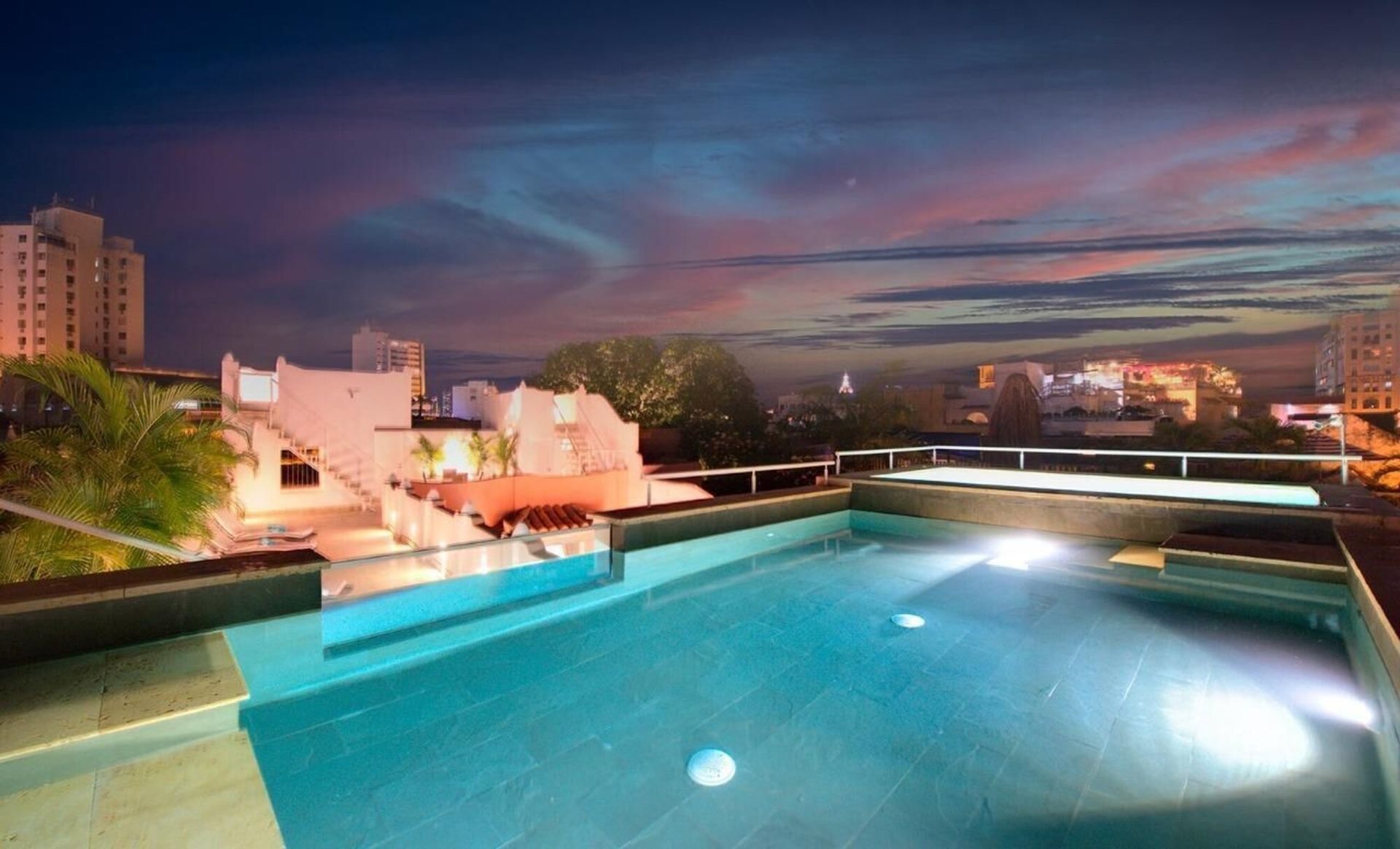 Una gran piscina está iluminada por la noche con una ciudad al fondo.