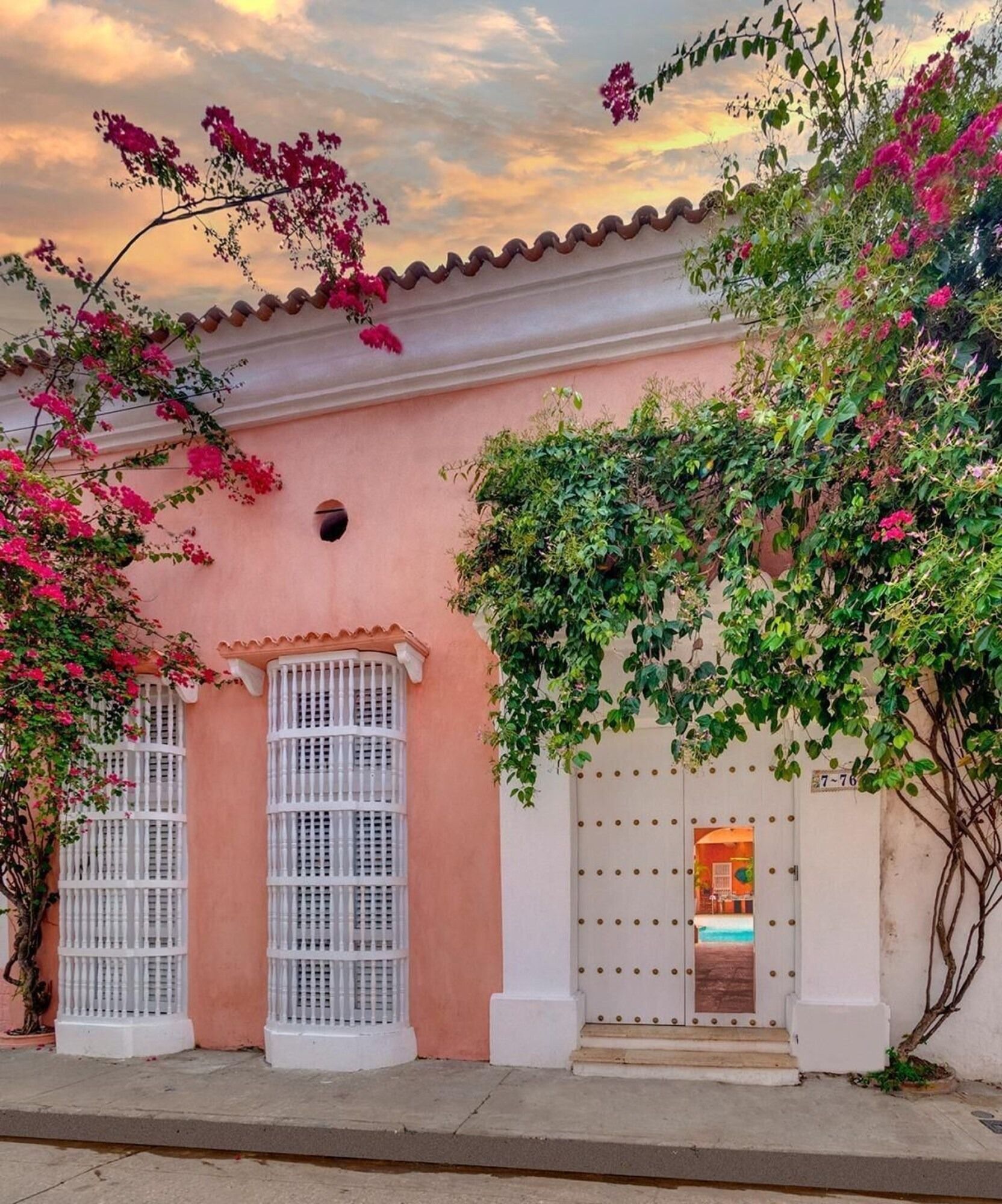 Un edificio rosa con ventanas blancas y un árbol delante.