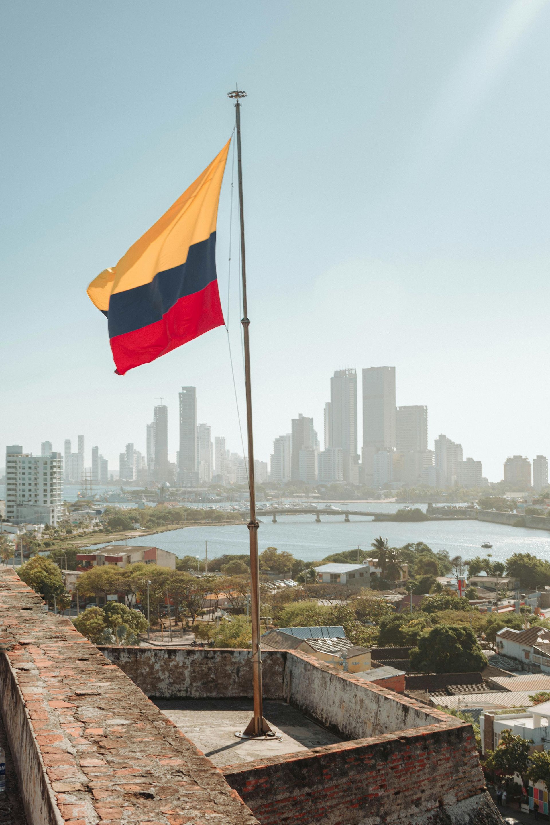 Una bandera colombiana ondea frente al horizonte de una ciudad.